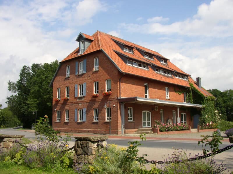 Die Okermühle von der Straßenseite: Backsteinfassade mit Blumenkästen, blauen Fensterläden und begrüntem Vorgarten